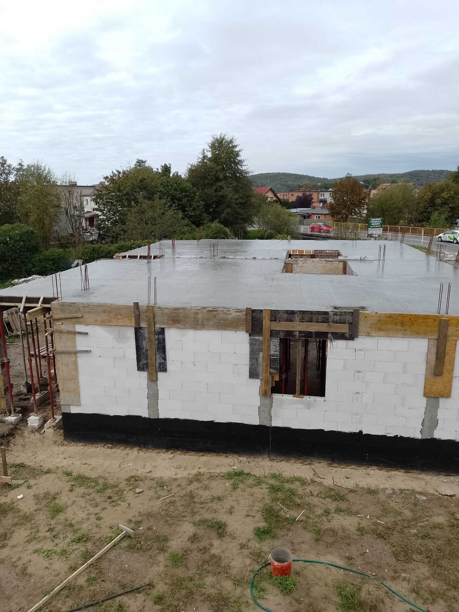 Wznoszenie ścian z bloczków białych, z widoczną izolacją fundamentów, szalunkiem okiennym i zalanym betonem stropem na budowie domu jednorodzinnego w trakcie realizacji.