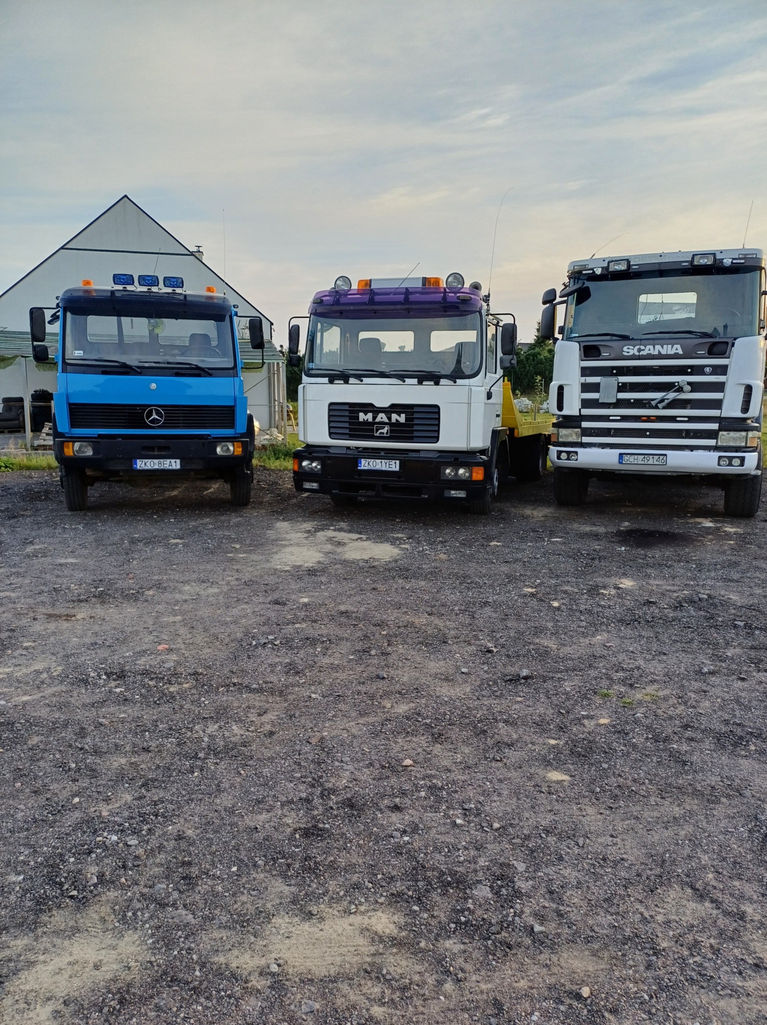 Trzy ciężarówki różnych marek (Mercedes, MAN, Scania) zaparkowane obok siebie na żwirowym placu w Sianowie, prawdopodobnie należące do firmy budowlanej.
