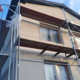 Dom w trakcie prac elewacyjnych, widoczne rusztowania i okna zabezpieczone folią, fragment dachu.