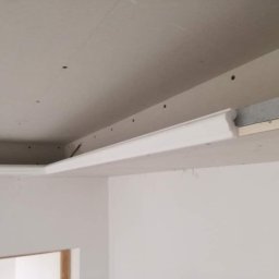 Maj-bud - Wnętrze w trakcie wykańczania: widoczna surowa konstrukcja sufitu podwieszanego z zamontowaną listwą ozdobną, ściany przygotowane do malowania.