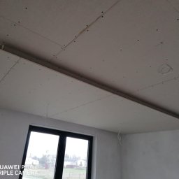 Maj-bud - Montaż podwieszanego sufitu z płyt gipsowo-kartonowych, widoczne łączenia i przewody elektryczne, okno w tle.