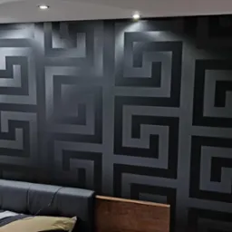 Czarna ściana w sypialni pokryta tapetą z geometrycznym wzorem meandry, widoczny klimatyzator i fragment łóżka.