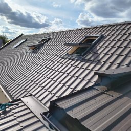 Maj-bud - Nowy, brązowy dach z dachówki modułowej i oknami dachowymi, widok z góry, na dachu leży dmuchawa akumulatorowa, obróbki blacharskie w kolorze dachu.