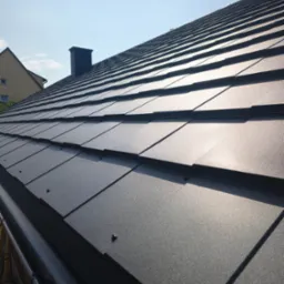 Nowy, grafitowy dach z blachodachówki modułowej w promieniach słońca, z widoczną rynną i kominem w tle. Detal łączenia arkuszy, minimalizm.