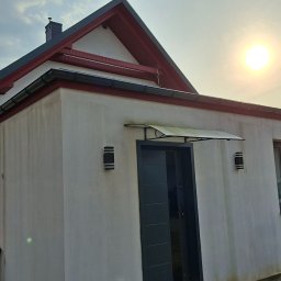 Maj-bud - Wykończony budynek z ocieploną elewacją, widoczne rynny, dach z czerwoną podbitką i nowoczesne oświetlenie zewnętrzne. Osoba przy budynku.