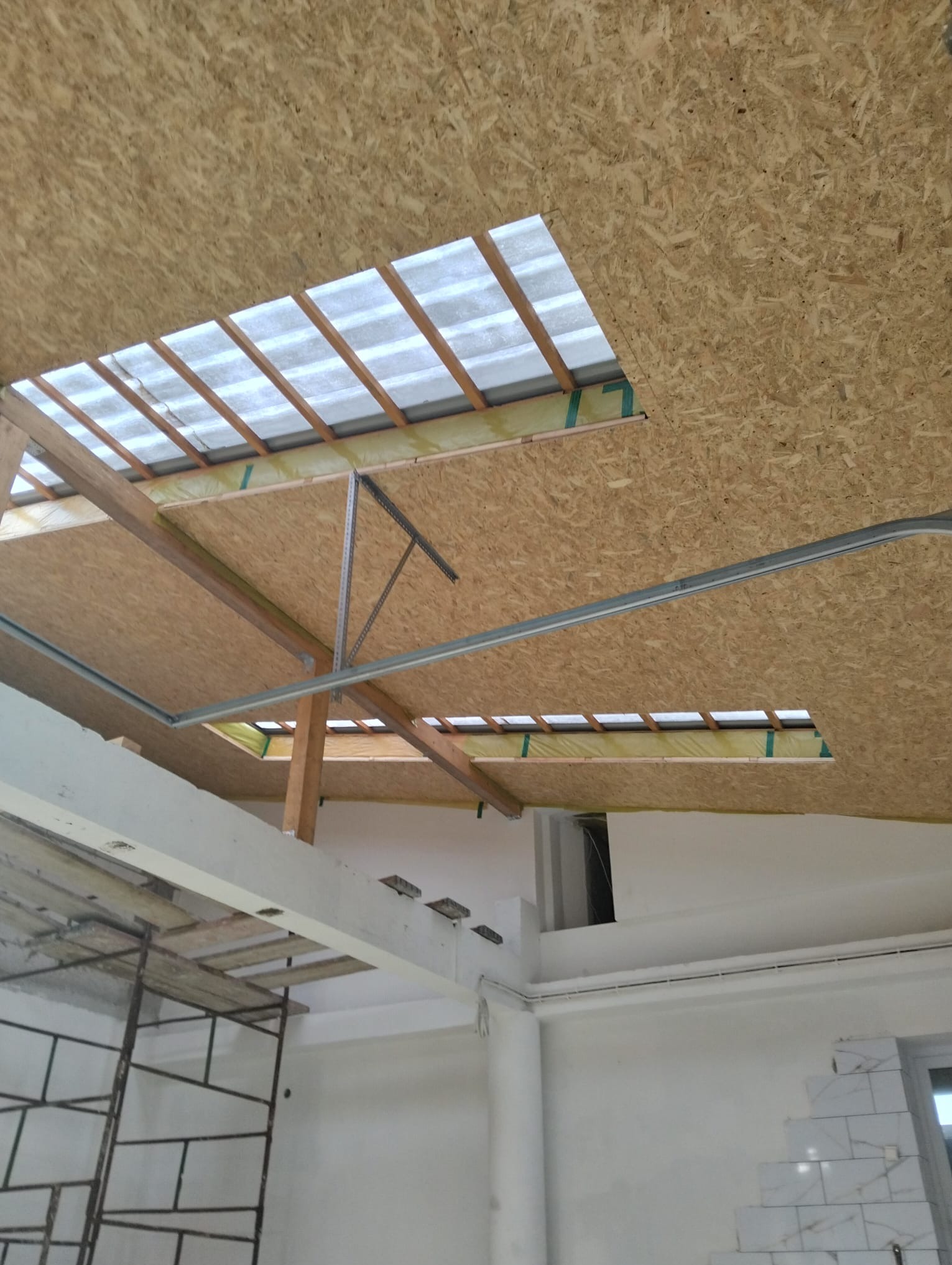 Płyta OSB na poddaszu z oknami dachowymi w trakcie montażu, widoczne elementy konstrukcyjne i rusztowanie. Prace wykończeniowe w jasnym wnętrzu.