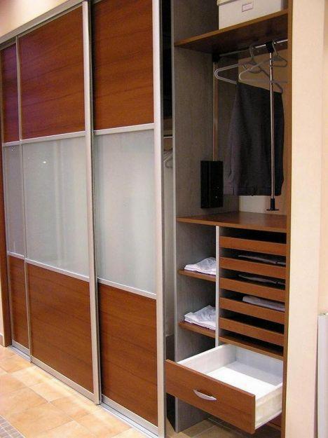 Wnętrze szafy przesuwnej z drewnianymi i matowymi szklanymi panelami, otwartą częścią z półkami i wysuwanymi szufladami.