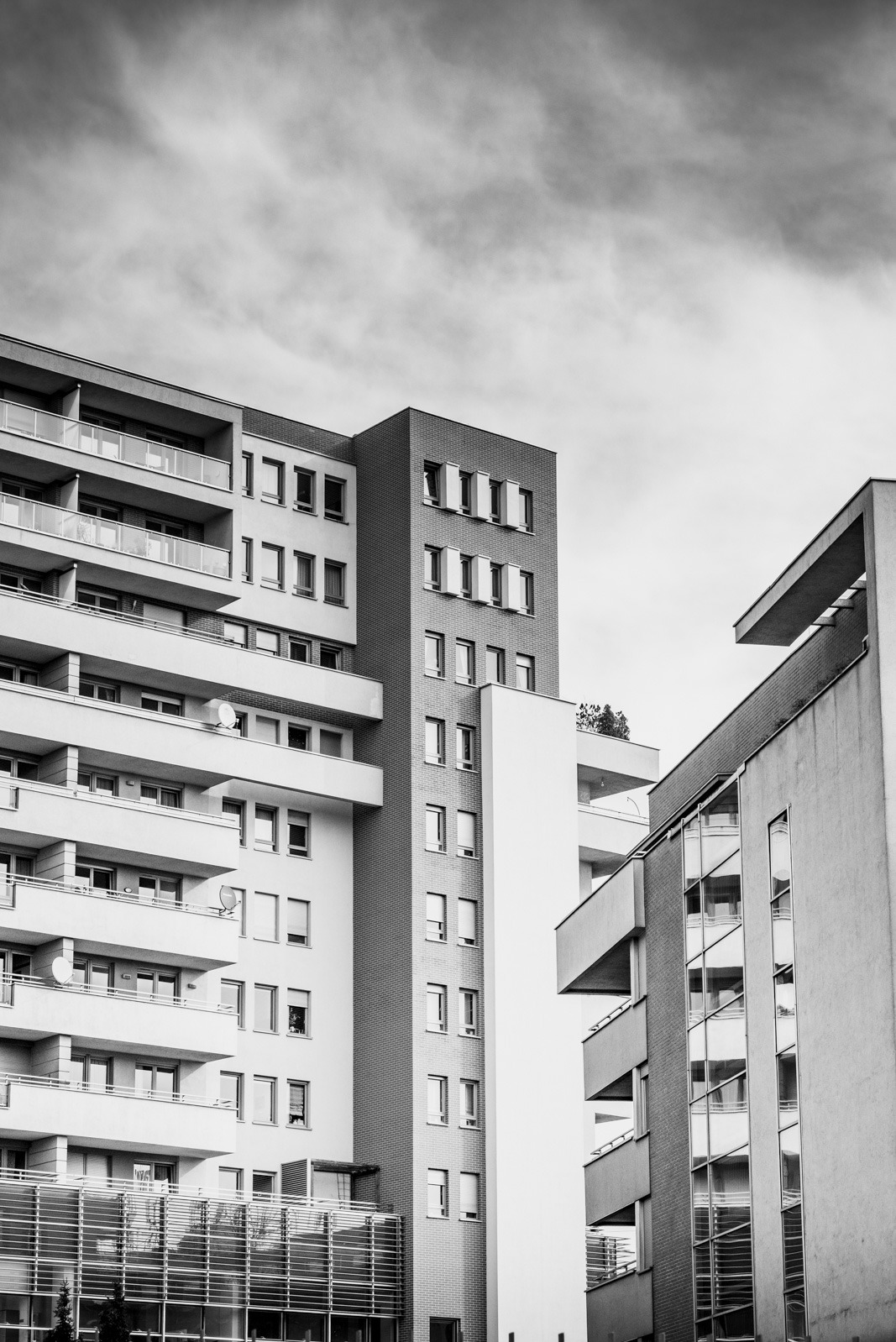 Monochromatyczne ujęcie z dołu na nowoczesne budynki mieszkalne z balkonami i dużymi oknami, na tle pochmurnego nieba. Minimalistyczna architektura.
