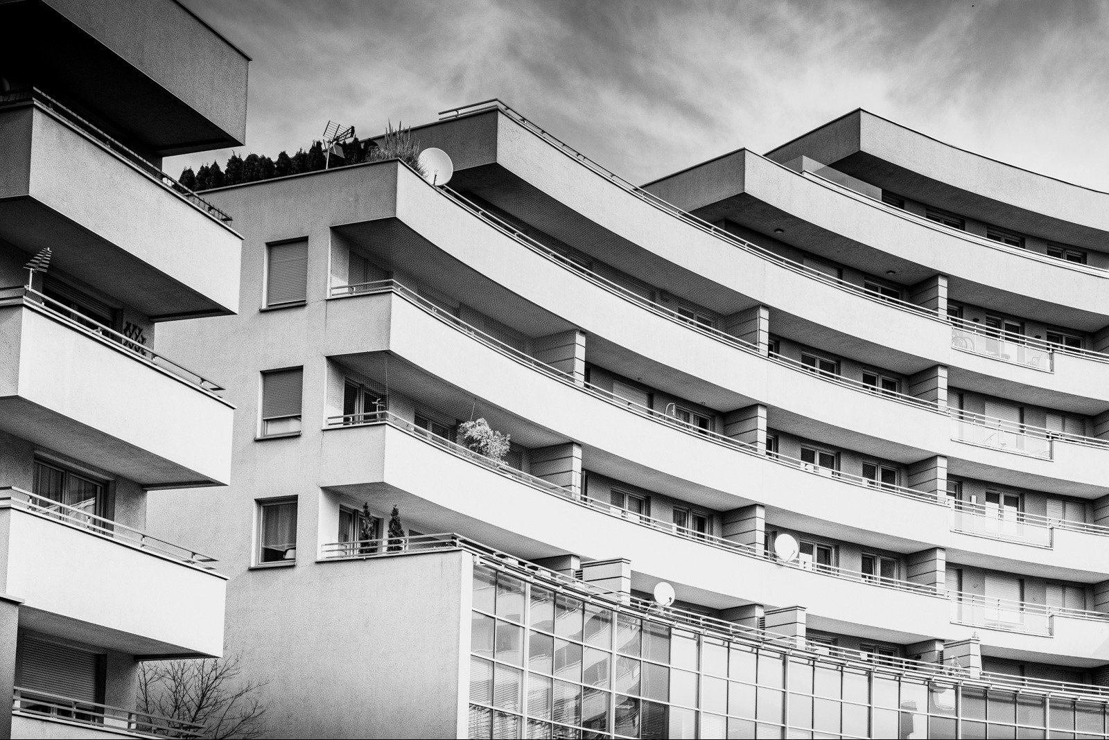 Czarno-białe zdjęcie fasady nowoczesnego budynku mieszkalnego z balkonami o zaokrąglonych kształtach i dużymi oknami, widzianego pod kątem od dołu.