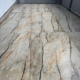 Gold Design Usługi remontowe - Wykończona podłoga na balkonie z szarych płytek imitujących marmur z ciemnymi żyłami. Metalowa balustrada z perforowanej blachy. Minimalistyczny design.