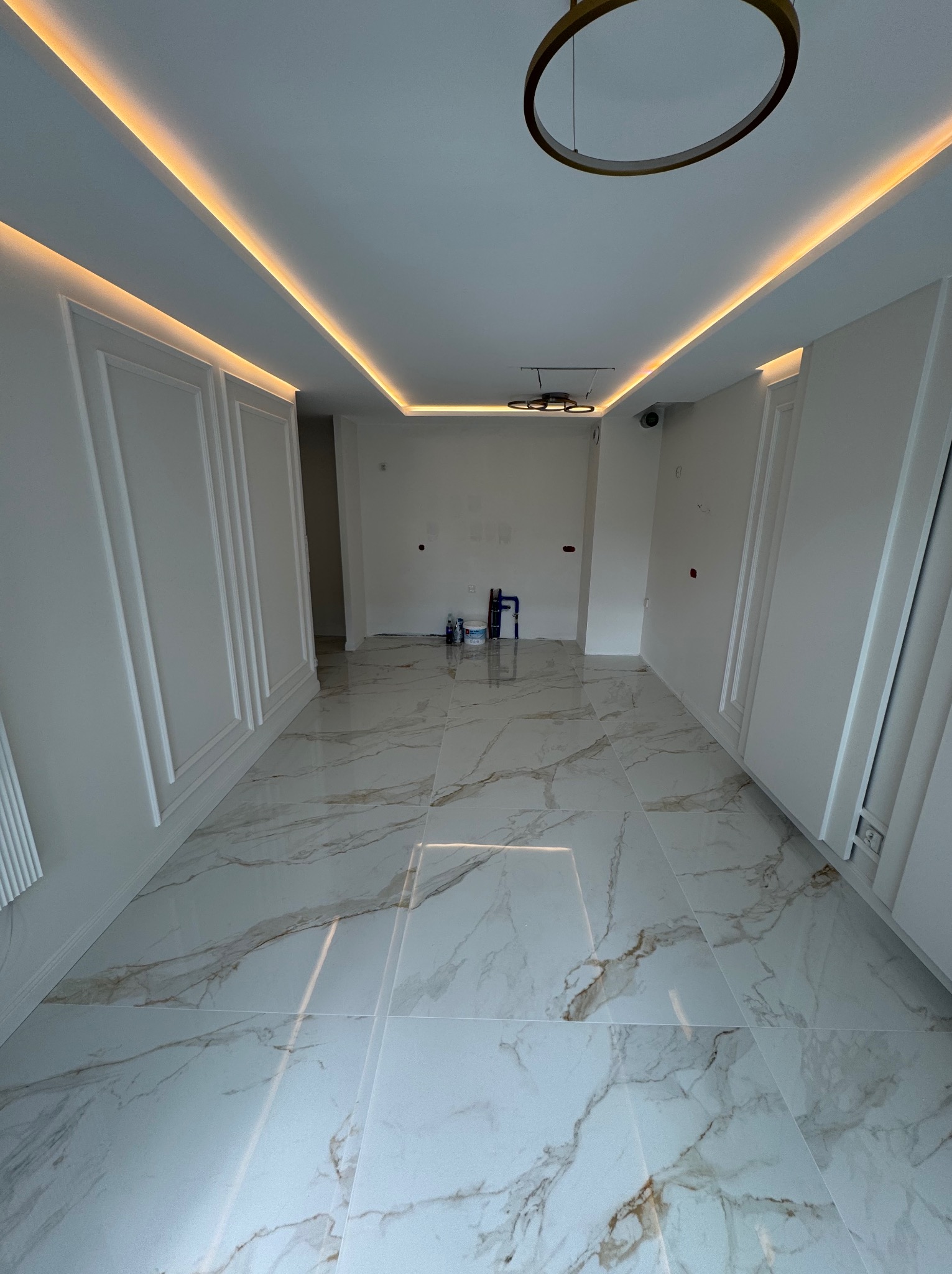 Eleganckie wnętrze po remoncie: białe ściany z dekoracyjnymi panelami, marmurowe płytki podłogowe, nowoczesne oświetlenie sufitowe. Estetyczne wykończenie.