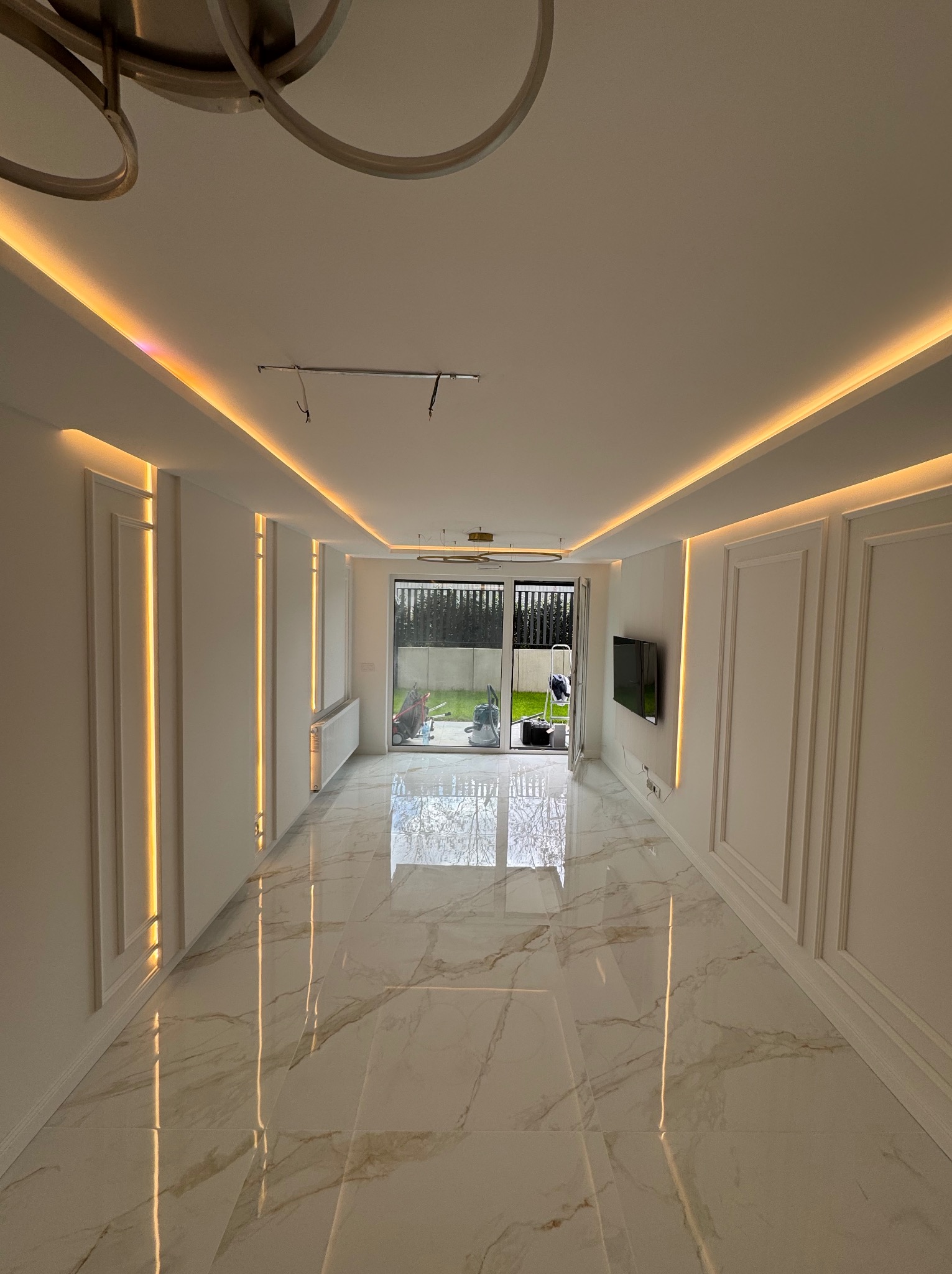 Eleganckie wykończenie wnętrza: białe ściany z dekoracyjnymi panelami, marmurowe płytki podłogowe z połyskiem i subtelne oświetlenie LED wzdłuż sufitu.