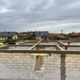 Wznoszenie ścian parteru z betonu komórkowego na fundamencie, widok z góry na budowę domu jednorodzinnego z żółtym samochodem dostawczym w tle.