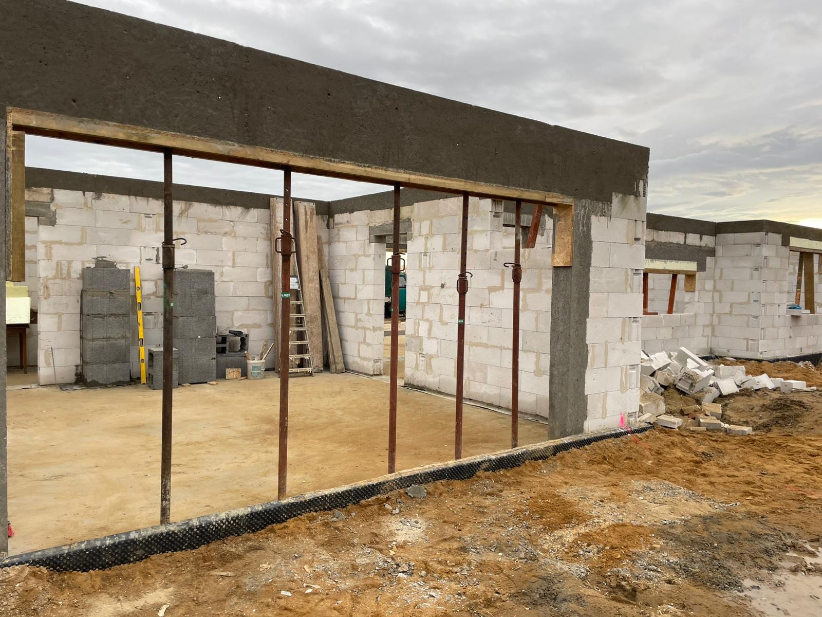 Wznoszenie ścian z białych bloczków na budowie domu, widoczne podpory stropowe, poziomica i paleta z bloczkami, grunt wokół budynku przygotowany pod dalsze prace.