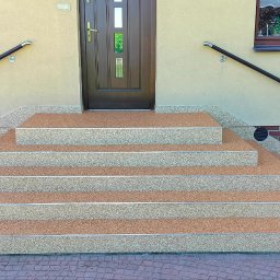 KWwork Kacper Wróbel - Schody wejściowe do domu wykończone żywicą epoksydową z kruszywem kwarcowym, tworzące wzór dywanu kamiennego, z metalowymi listwami na krawędziach stopni.