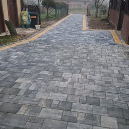 BRUKO-BUD MATEUSZ KOBYLSKI - Ułożona ścieżka z szarej kostki brukowej z żółtymi obrzeżami, prowadząca przez posesję w mglisty dzień.