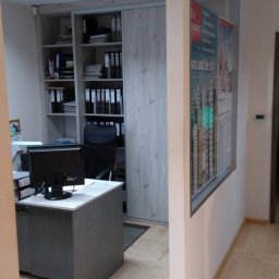 KANCELARIA DORADCY PODATKOWEGO BIURO RACHUNKOWE Paweł Kruszyński - Biuro z biurkiem, komputerem i regałem wypełnionym segregatorami, widoczne plakaty na ścianie.