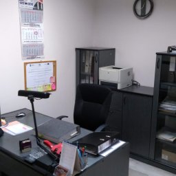 KANCELARIA DORADCY PODATKOWEGO BIURO RACHUNKOWE Paweł Kruszyński - Biuro z czarnymi meblami, kalendarzem na ścianie i biurkiem z dokumentami, kalkulatorem i lampką.