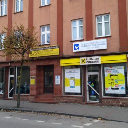 KANCELARIA DORADCY PODATKOWEGO BIURO RACHUNKOWE Paweł Kruszyński - Budynek z biurami usługowymi, w tym Kancelaria Doradcy Podatkowego i Biuro Rachunkowe z żółtym szyldem, obok Raiffeisen Polbank i fryzjer męski, na ulicy z drzewem i zaparkowanym samochodem.