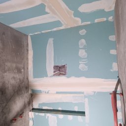 sucha_zabudowa.slowinski - Niedokończona łazienka w trakcie remontu: ściany i sufit z niebieskich płyt gipsowo-kartonowych z widocznymi łączeniami zaszpachlowanymi na biało, surowa betonowa podłoga, widoczne instalacje wodne...