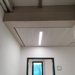 sucha_zabudowa.slowinski - Wykończony sufit podwieszany z oświetleniem w Chocianowicach. Widoczne instalacje i fragment ściany z oknem. Minimalistyczny design, jasne wnętrze.