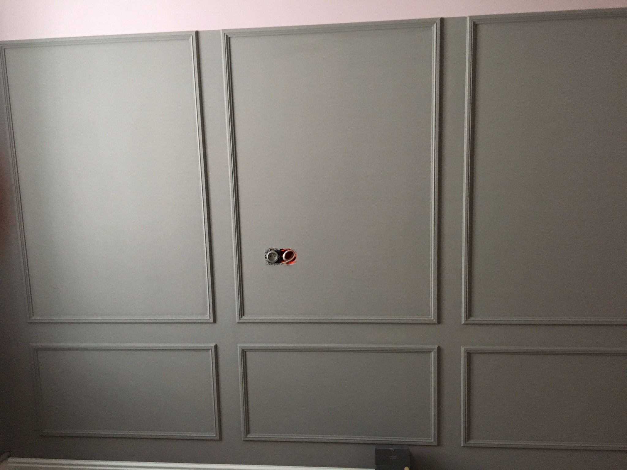 Szara ściana z dekoracyjnymi panelami i gniazdkiem elektrycznym w trakcie montażu, widok z bliska. Element wykończenia wnętrza.