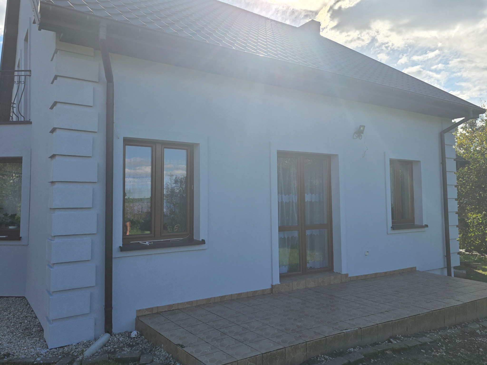 Biały dom jednorodzinny z brązowymi oknami i ciemnym dachem, widok z zewnątrz, elewacja z dekoracyjnymi elementami architektonicznymi.