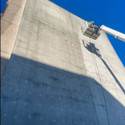 Paweł Pyrek - Pracownik w podnośniku koszowym myje elewację wysokiego budynku, widoczne plamy na ścianie i ślady po myciu.