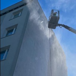 Paweł Pyrek - Mycie elewacji budynku w Gdyni za pomocą myjki ciśnieniowej z podnośnika koszowego na tle błękitnego nieba.