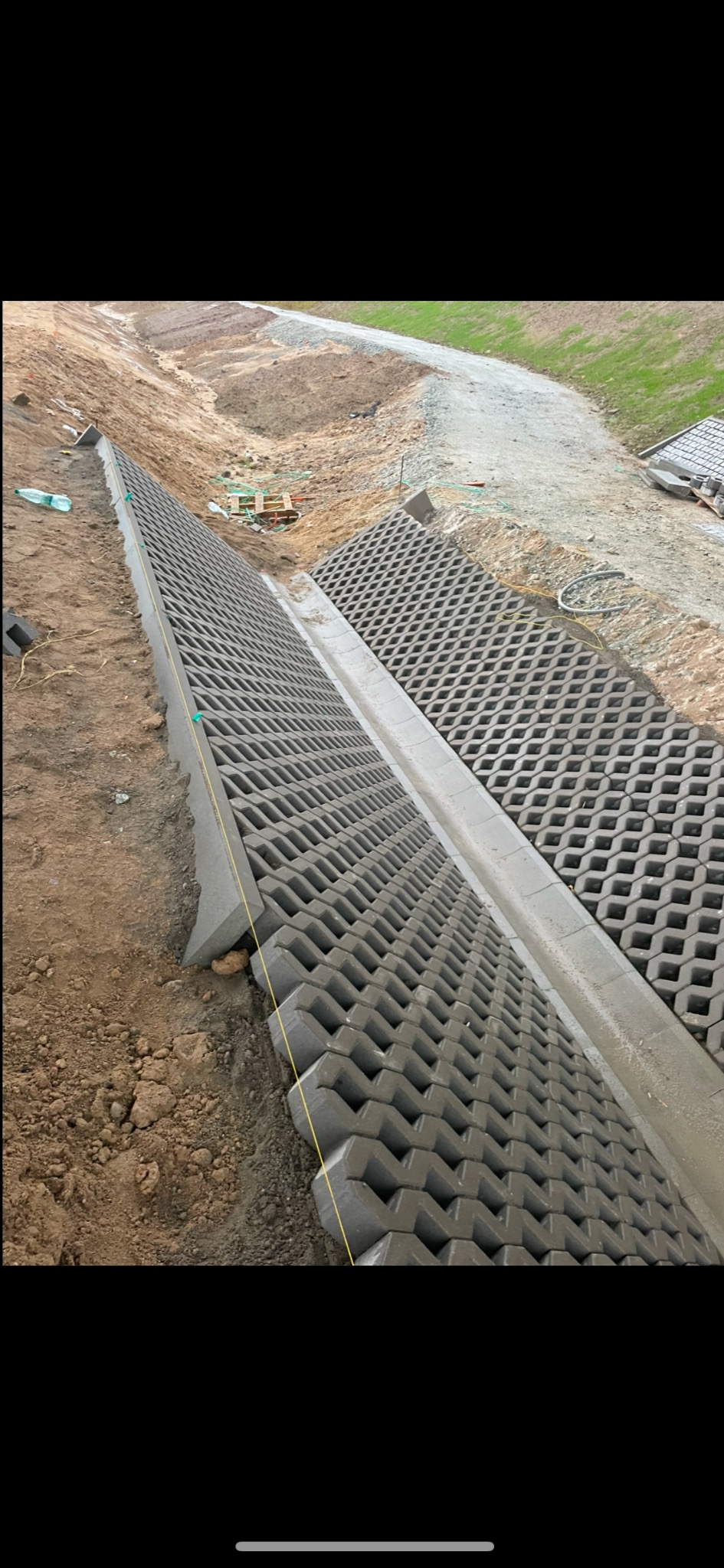 Układanie ażurowych płyt betonowych na skarpie, widoczna żółta nić poziomująca, grunt ziemny w tle.