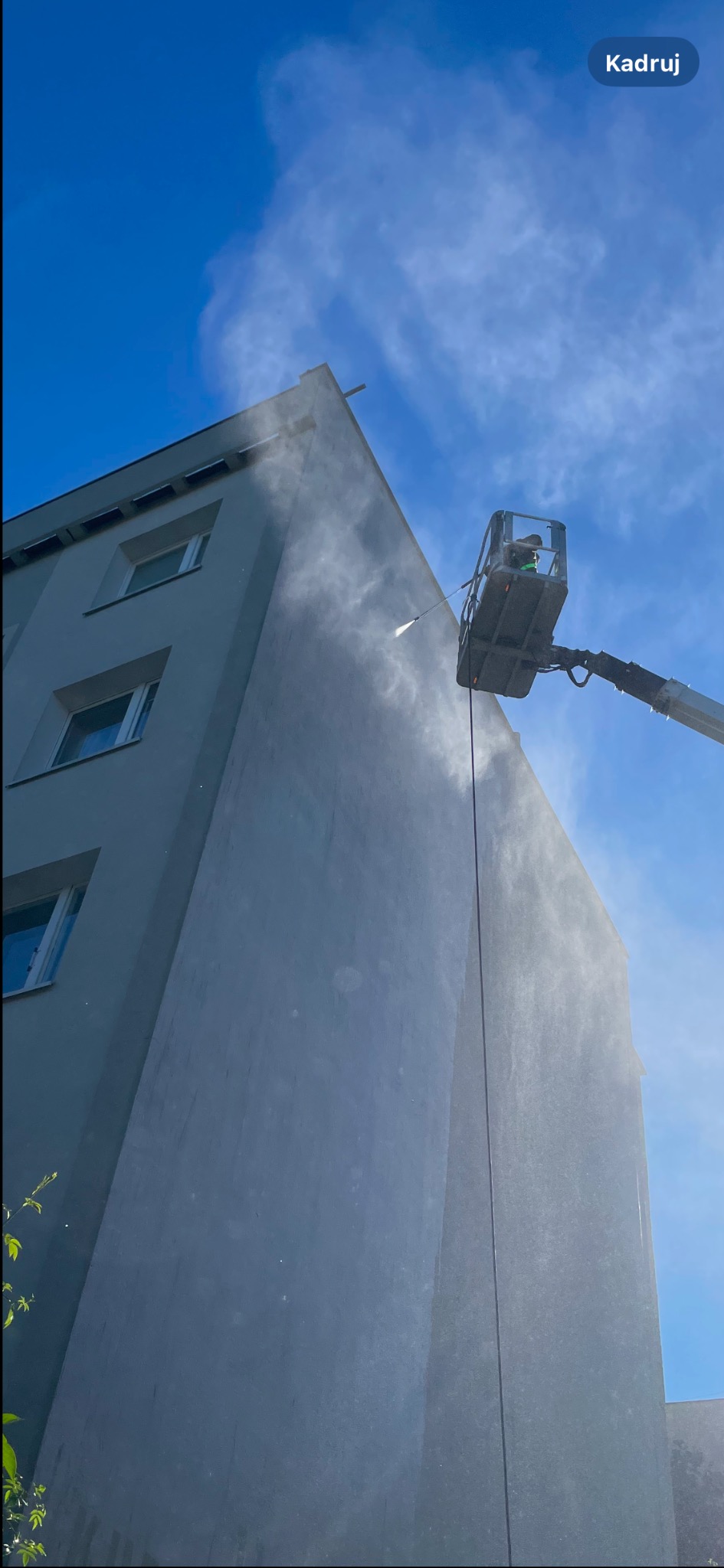 Mycie elewacji budynku w Gdyni za pomocą myjki ciśnieniowej z podnośnika koszowego na tle błękitnego nieba.