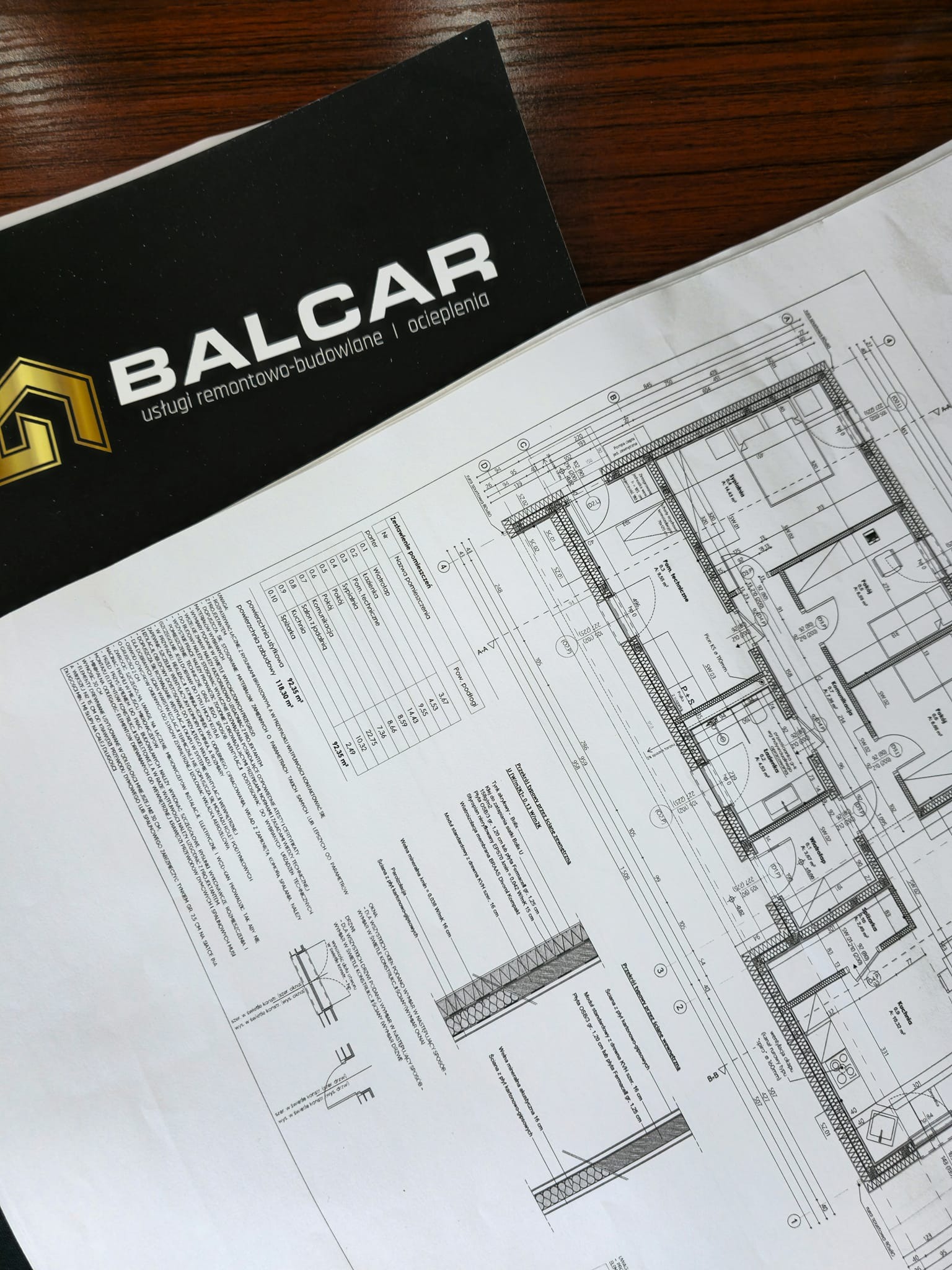 Plan architektoniczny domu z zestawieniem pomieszczeń i przekrojem ściany, obok wizytówka firmy remontowo-budowlanej BALCAR.