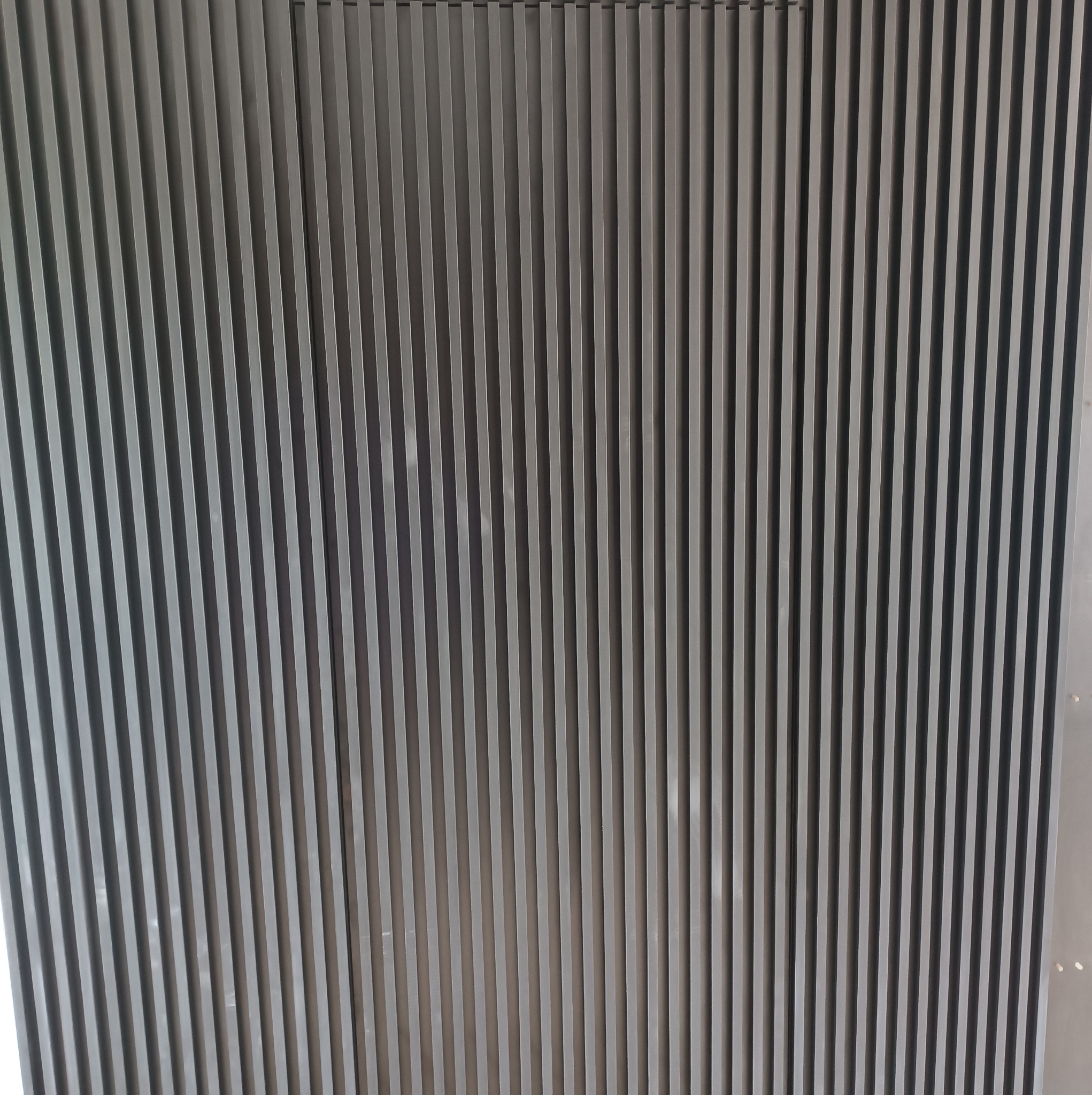 Szare lamele dekoracyjne zamontowane pionowo na ścianie, tworzące rytmiczny wzór.