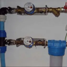 Węzeł wodomierzowy z filtrem mechanicznym, zaworami i rurami z tworzyw sztucznych wewnątrz szafki, widoczne dwa liczniki zużycia wody.