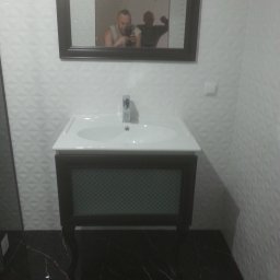 Zdzisław Hamerski - Nowoczesna łazienka z czarną marmurową podłogą i białą umywalką z szafką w ciemnej ramie; w lustrze odbija się osoba robiąca zdjęcie i druga osoba.