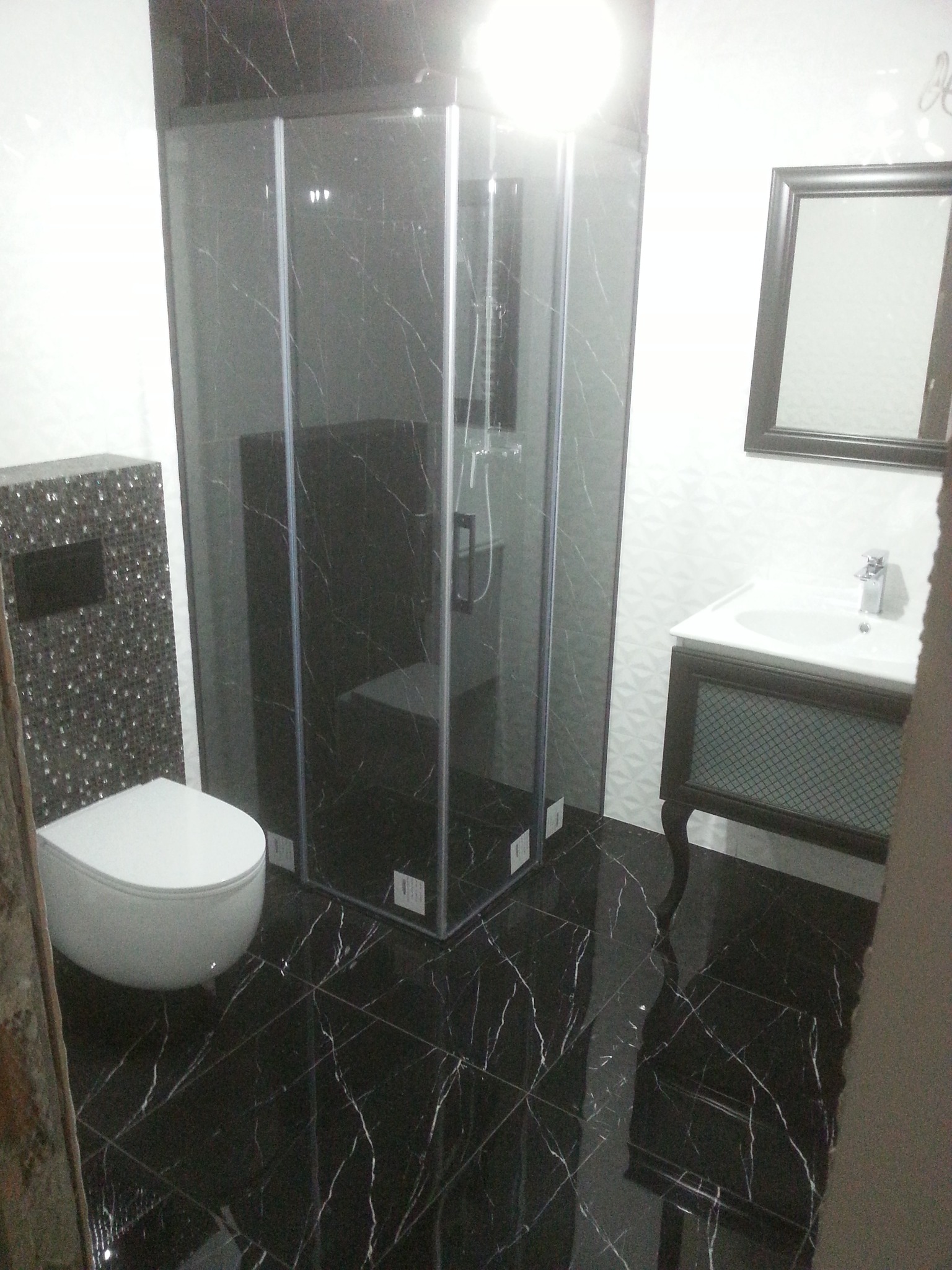 Wykończona łazienka z czarną marmurową podłogą i kabiną prysznicową, toaleta z mozaiką i umywalką z lustrem.