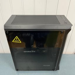 Komputeron - Serwis komputerowy - Komputer stacjonarny w czarnej obudowie z widoczną kartą graficzną GeForce RTX i naklejką ostrzegawczą na szklanym panelu bocznym.