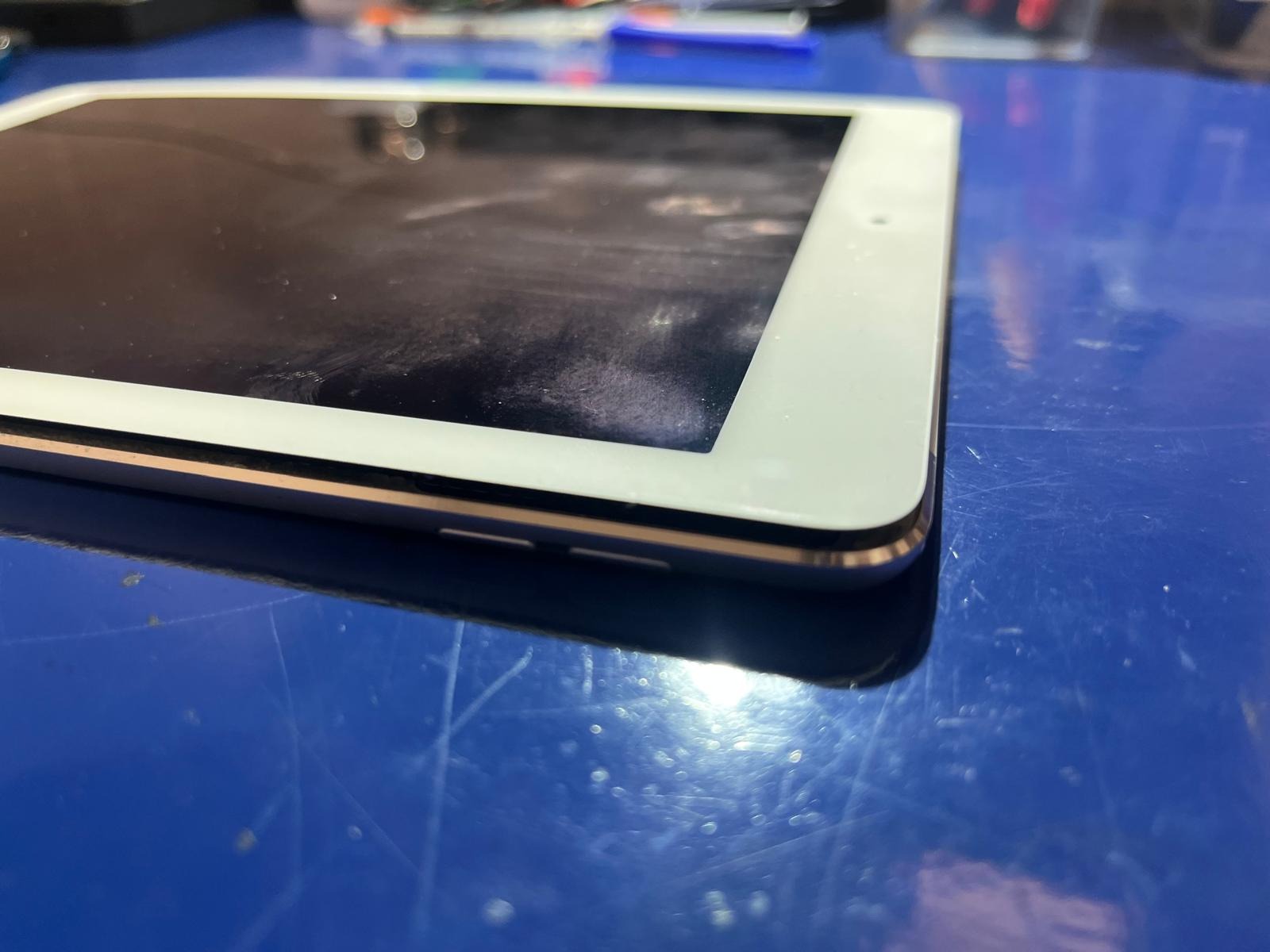 Tablet z widocznymi śladami użytkowania leżący na niebieskim blacie zarysowanym drobnymi rysami.