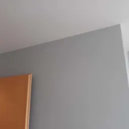 Świeżo pomalowana szara ściana w pokoju, widoczny fragment ościeżnicy drewnianych drzwi.