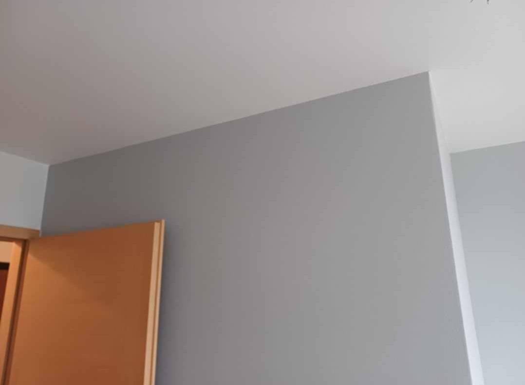 Świeżo pomalowana szara ściana w pokoju, widoczny fragment ościeżnicy drewnianych drzwi.