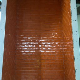 Henzbud - Pomarańczowe, błyszczące płytki ułożone w cegiełkę na ścianie wnęki, obudowane płytą gipsową. Widoczne metalowe profile konstrukcyjne.