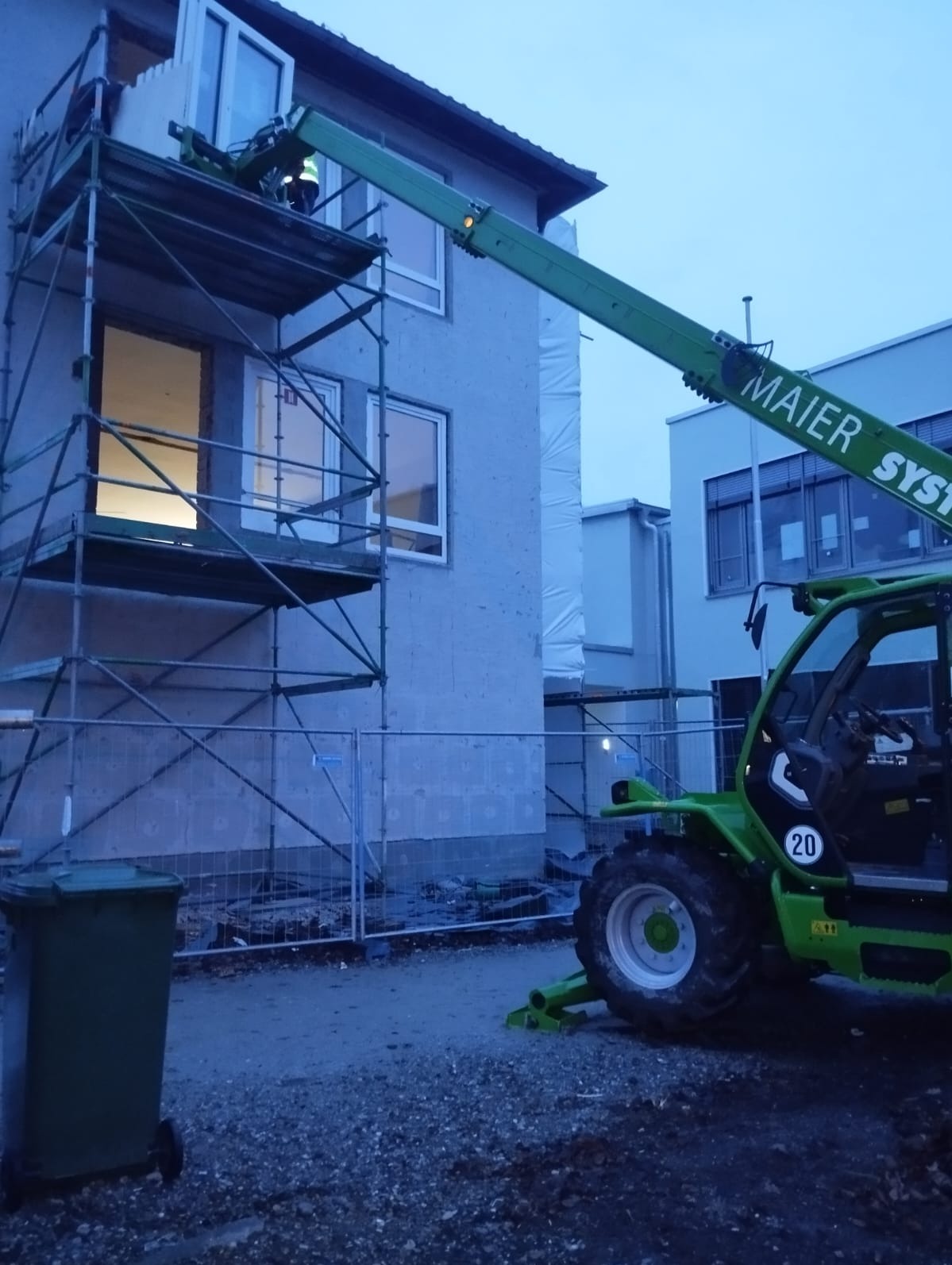 Montaż okna na rusztowaniu przy użyciu podnośnika teleskopowego Maier System na tle budynku w trakcie budowy.