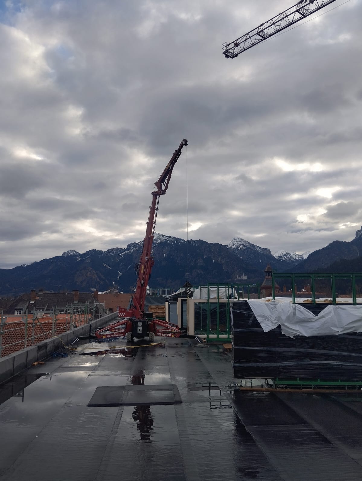 Montaż okien na dachu budynku za pomocą dźwigu, widoczne okna w ramie, góry w tle, pochmurne niebo.