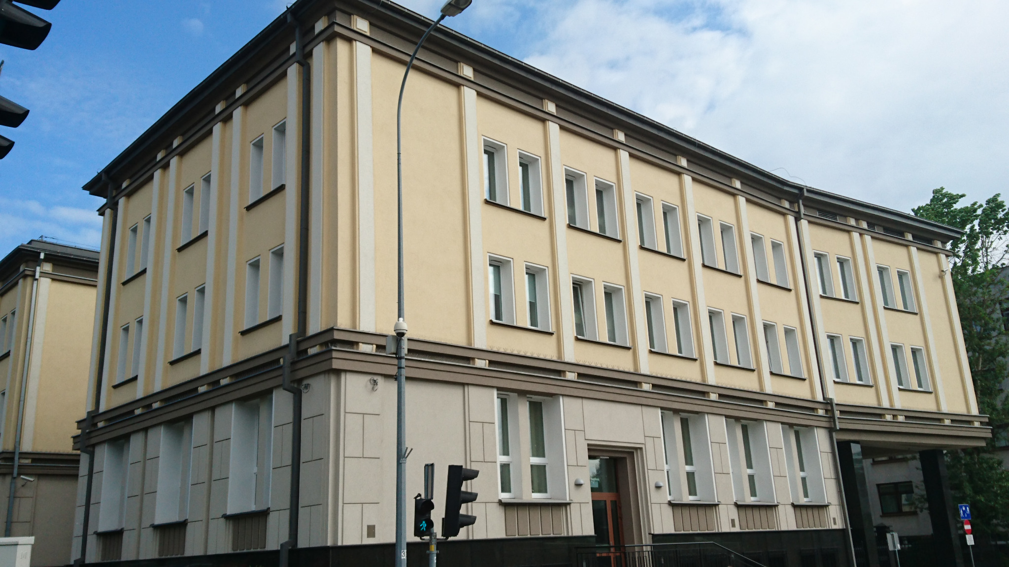 Odnowiony budynek biurowy z beżową elewacją, białymi obramowaniami okien i szarym cokołem, widziany z poziomu ulicy, z sygnalizacją świetlną w pierwszym planie.