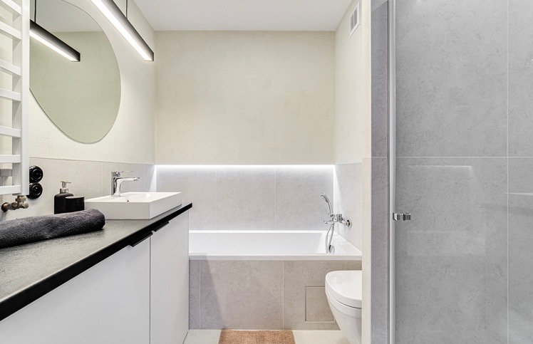 Nowoczesna łazienka z wanną, umywalką nablatową, okrągłym lustrem z podświetleniem LED i szarymi płytkami.