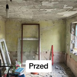 Renovation&You - Wnętrze pokoju przed remontem: zniszczone ściany z odpadającą farbą, surowy otwór okienny, okna wstawione do pokoju, narzędzia i materiały budowlane w nieładzie, wisząca żarówka.