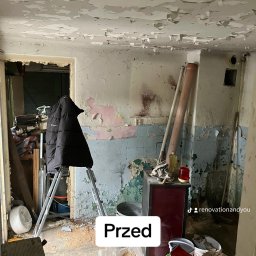 Renovation&You - Pokój przed remontem: odpadająca farba na ścianach i suficie, drabina z kurtką, piec, gruz i narzędzia na podłodze.