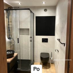 Renovation&You - Nowoczesna łazienka z czarną armaturą: kabina prysznicowa z deszczownicą, umywalka nablatowa na szafce, wisząca toaleta i czarne akcesoria na tle płytek imitujących kamień.