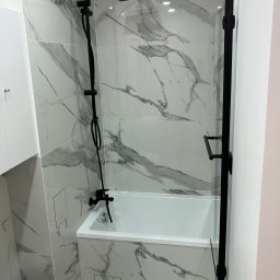 Renovation&You - Nowoczesna łazienka z wanną obudowaną płytkami imitującymi marmur, czarna armatura i szklany parawan nawannowy.