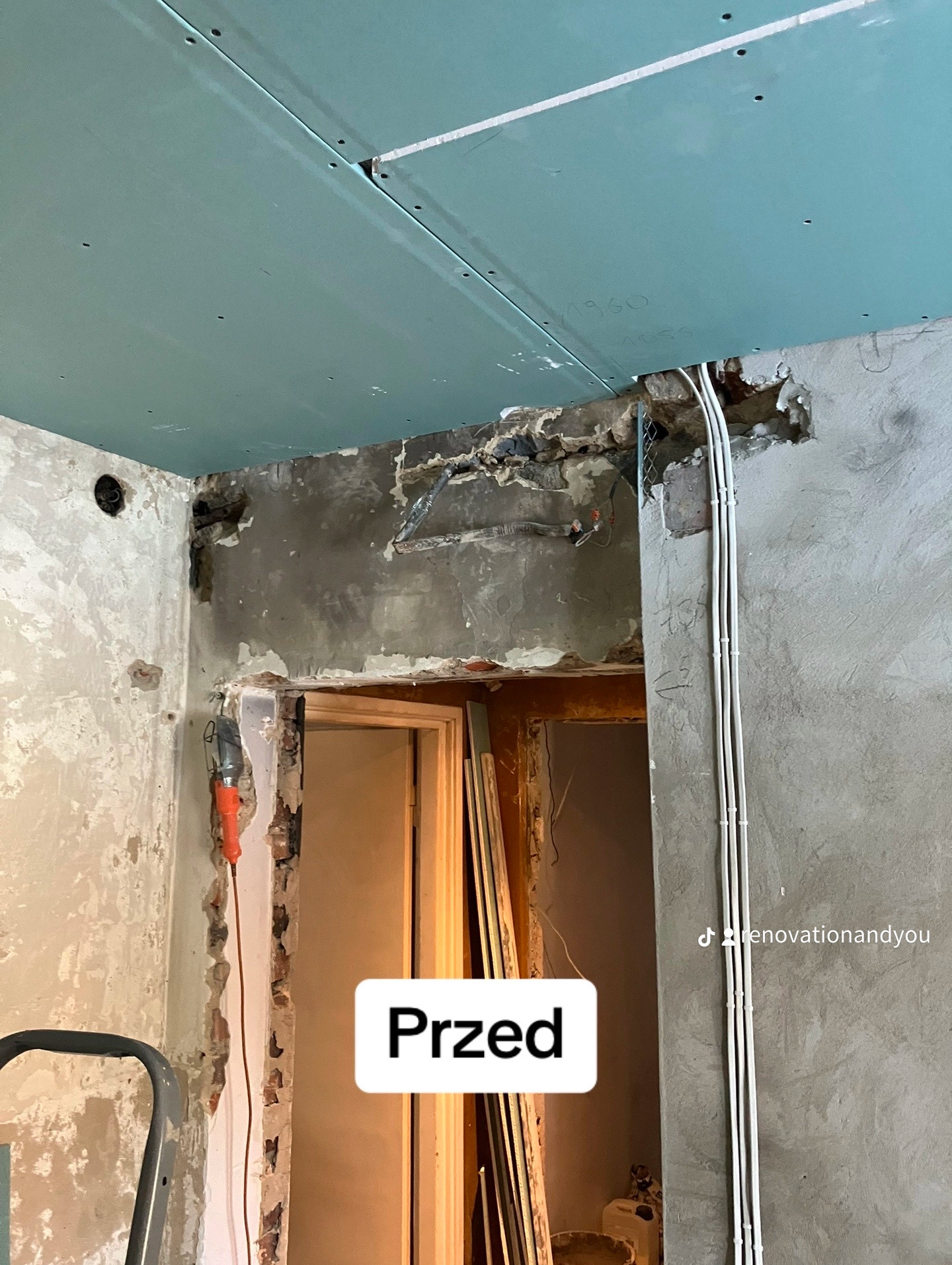 Zdjęcie przedstawia wnętrze w trakcie przygotowania do remontu: widoczne ściany z usuniętą warstwą wykończeniową, częściowo zamontowana płyta kartonowo-gipsowa na suficie, wystające przewody...